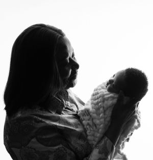 Black and white silhouette of mother and newborn baby wrapped in blanket gazing at each other in tender moment.
