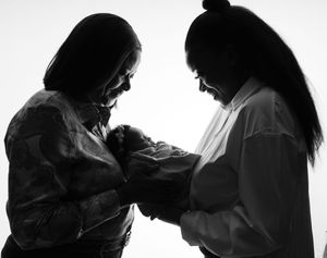 A black and white silhouette of two people looking down adoringly at a newborn baby in their arms.