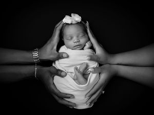 A series of black and white photos showing a newborn baby being gently cradled in caring hands.