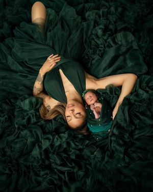 Two people laying on emerald green tulle fabric in elegant artistic portrait composition.