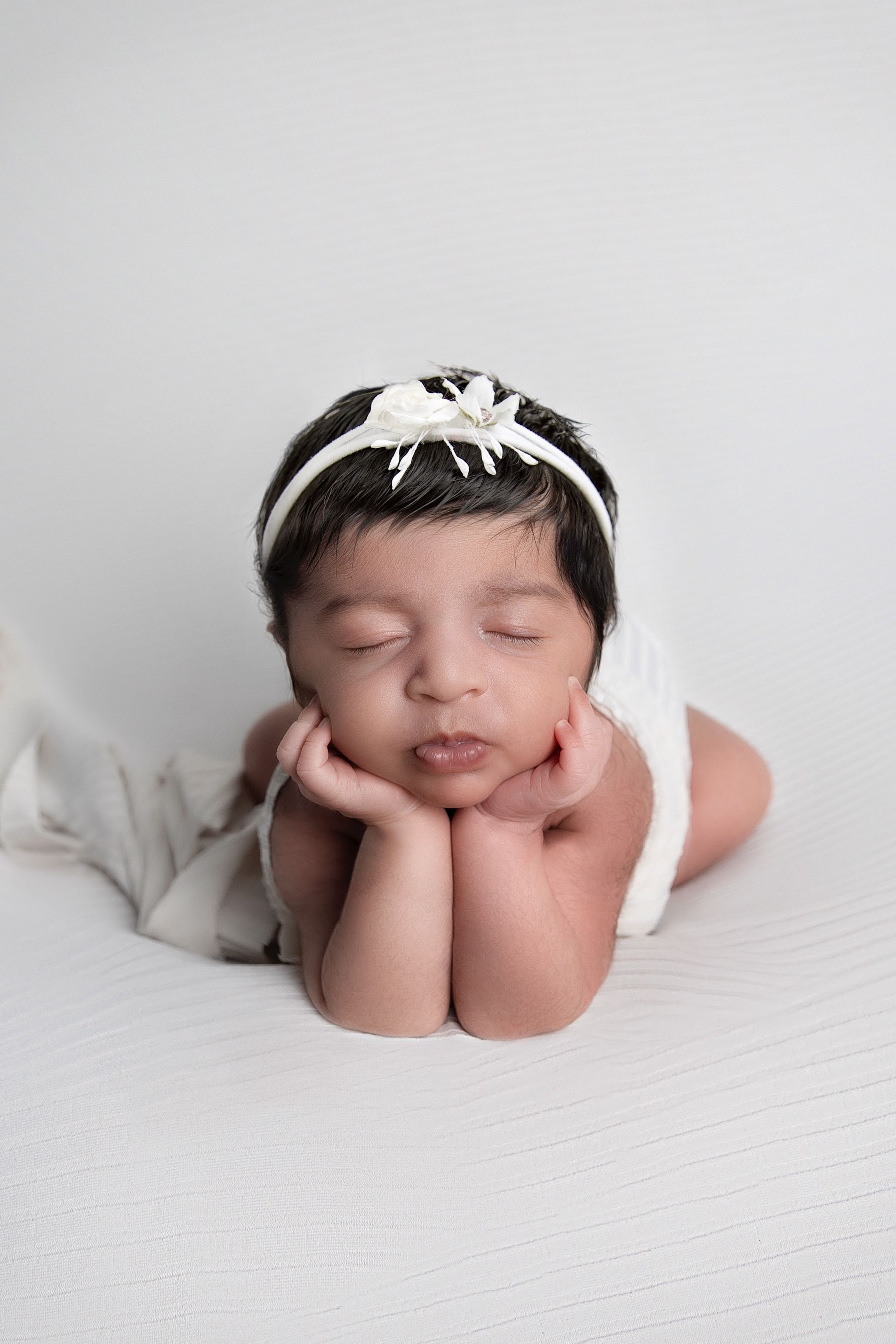 Luxury Newborn baby photoshoot, Vanessa Charlotte photography. Birmingham  Sleeping newborn in white headband rests with hands under chin.