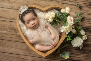 A series of baby photos with rustic wooden elements and delicate white roses arranged in a heart-shaped bowl.