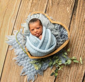 Newborn baby wrapped in soft blue blanket lying on wooden surface with delicate floral decorations.