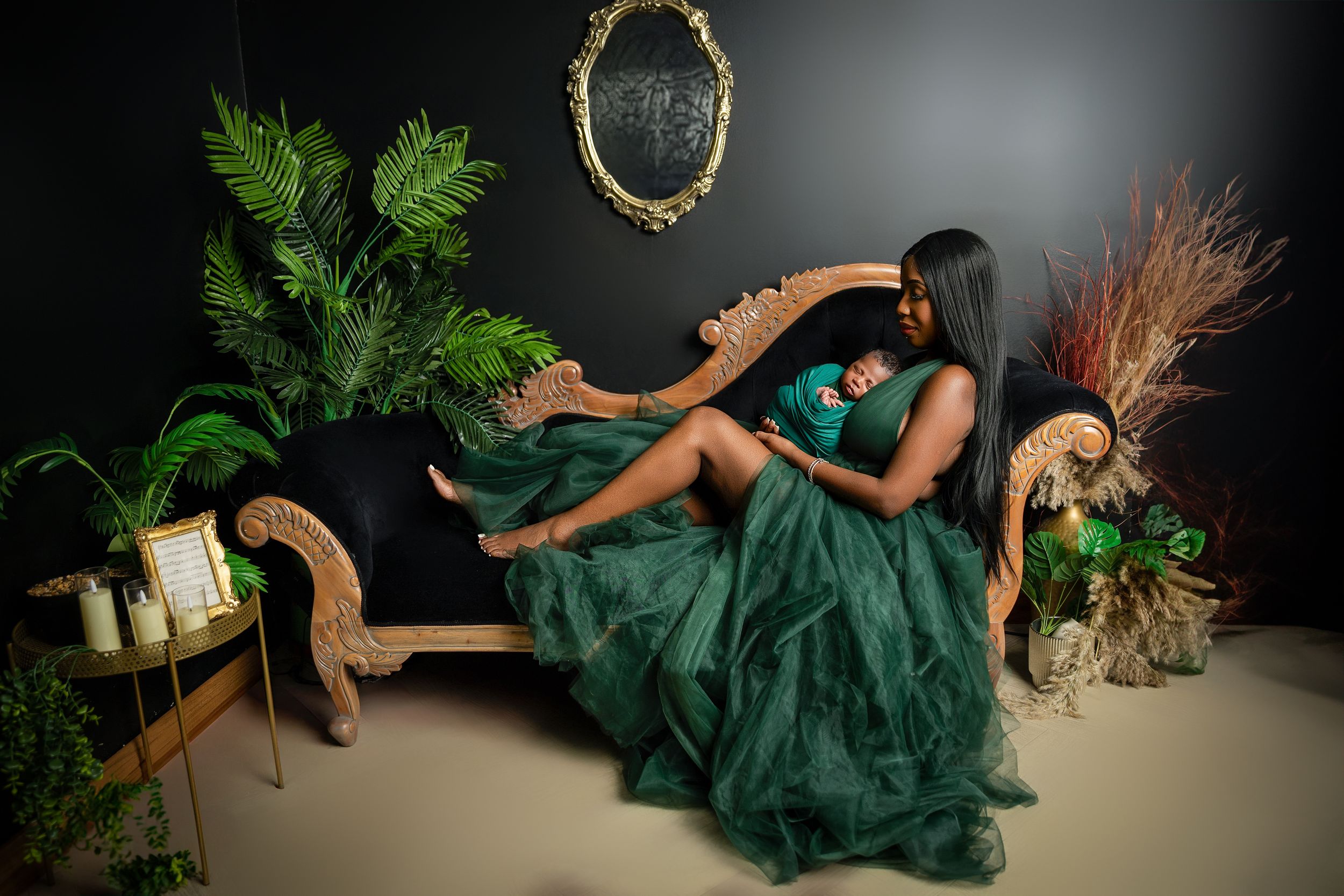 Elegant emerald green gown flows across vintage furniture amidst lush greenery and decor against a dark backdrop.