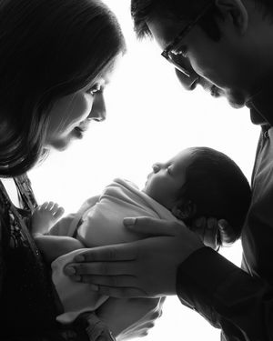 A tender black and white silhouette of new parents gazing lovingly at their baby together.