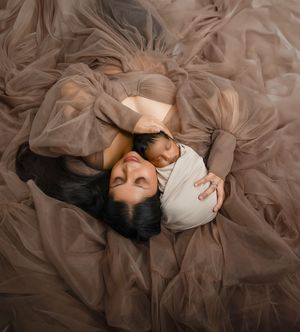 Two figures lying down together in a dreamy setting surrounded by flowing taupe tulle fabric in soft lighting.