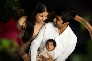 Family in white outfits pose together against dark background with red bokeh and greenery.