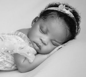 A sleeping baby in a white lace dress wearing a delicate headband rests peacefully in black and white.