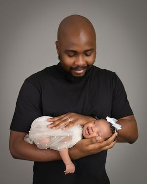 A loving parent in a black shirt tenderly holds and interacts with a baby wearing white lace clothing.