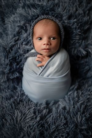 Newborn photography series showing baby wrapped in light gray swaddle against dark gray fluffy backdrop.
