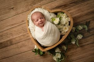 A series of newborn photography shots on wooden backdrop with white wraps and floral decorations.