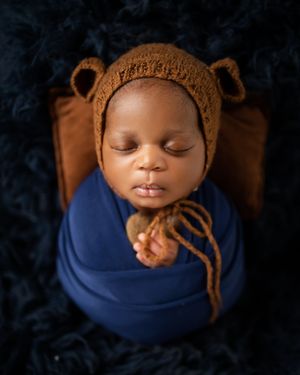 A sleeping baby in a blue wrap nestled against a dark background creates a serene newborn portrait series.