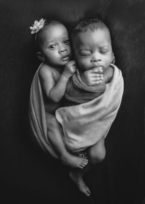 Heartwarming black and white portrait of two children sharing a tender moment while wrapped in soft fabric together.