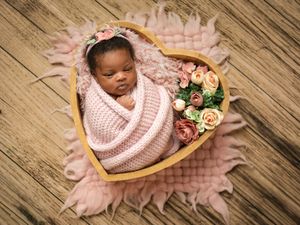 Wooden heart-shaped tray with pink knitted blanket and delicate floral decorations on rustic wooden floor.