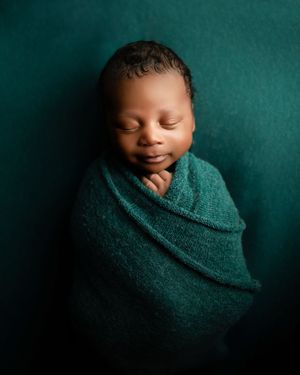 Sleeping newborn wrapped in teal blanket against matching teal backdrop in peaceful professional portrait.