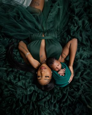 Two figures in dark green dresses lying on emerald-colored textured fabric creating an artistic overhead portrait.