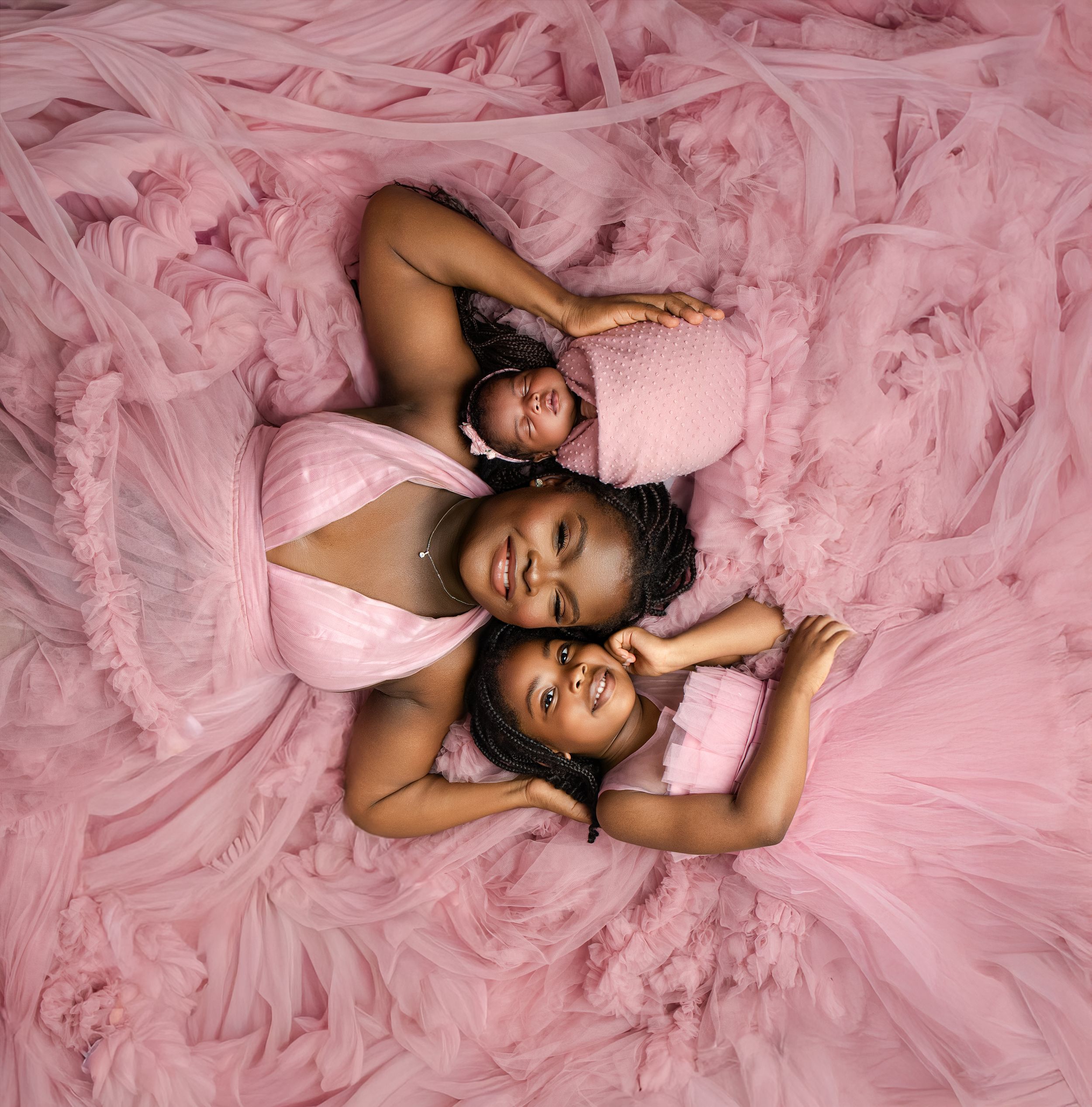 Young girl in flowing pink tulle dress poses gracefully on studio floor with pink backdrop.