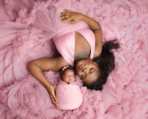 A tender moment captured between mother and baby lying on pink tulle fabric in coordinating pink outfits.