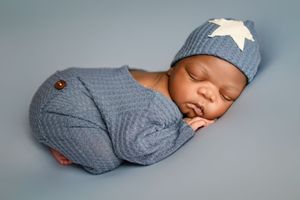 A sleeping newborn in a gray knit onesie with star details lying on a soft blue backdrop.