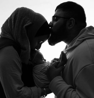 A silhouetted couple wearing glasses and hijab share an intimate moment while embracing in black and white.