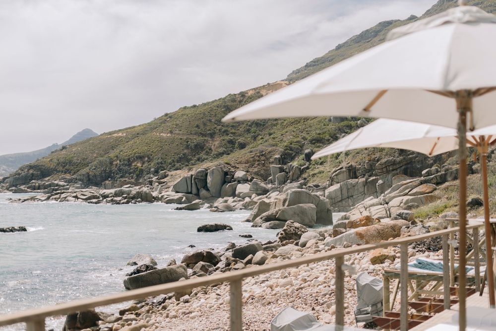 Rocky coastline with white beach umbrellas, turquoise ocean, and green hillside views.