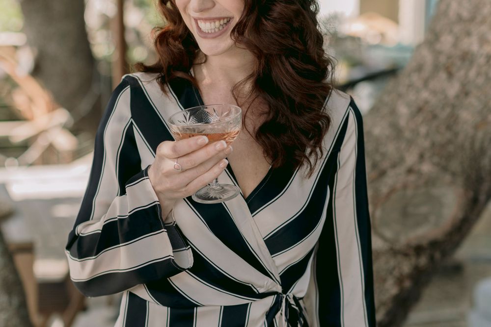 Smiling woman in striped dress holding a martini cocktail glass outdoors.