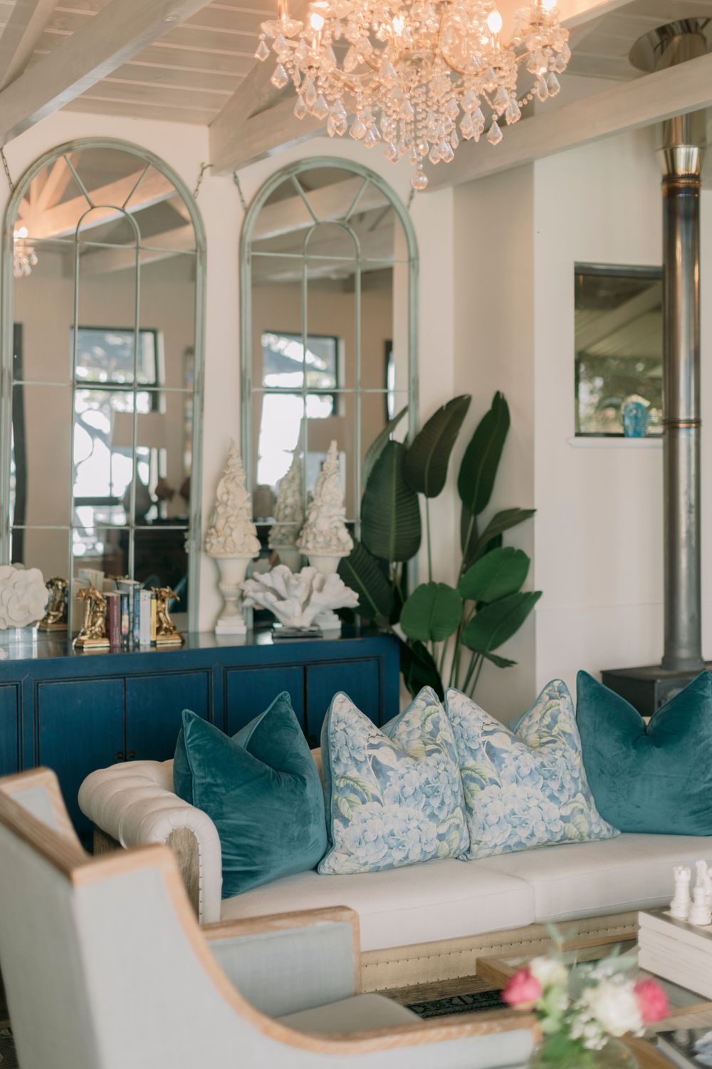Elegant living room with crystal chandelier, teal velvet pillows, and arched mirrors.