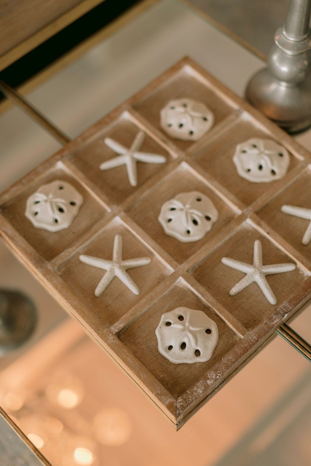 Decorative tic-tac-toe board game with starfish and sand dollar pieces on glass table.