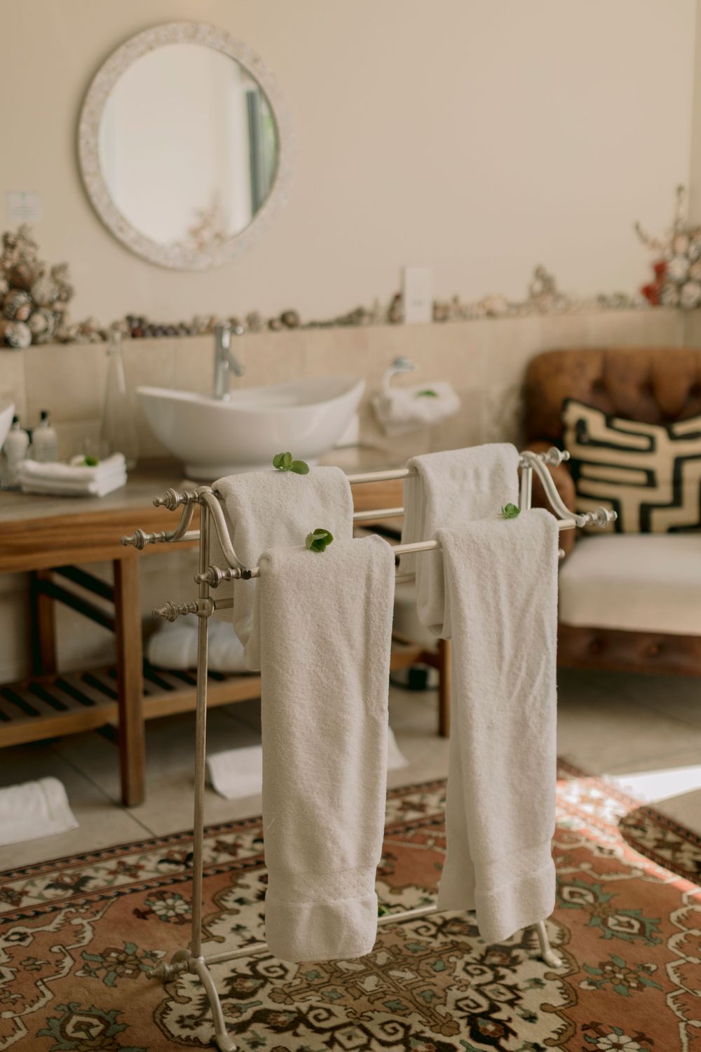 Spa bathroom with white towels on chrome rack, vessel sink, and vintage patterned rug.