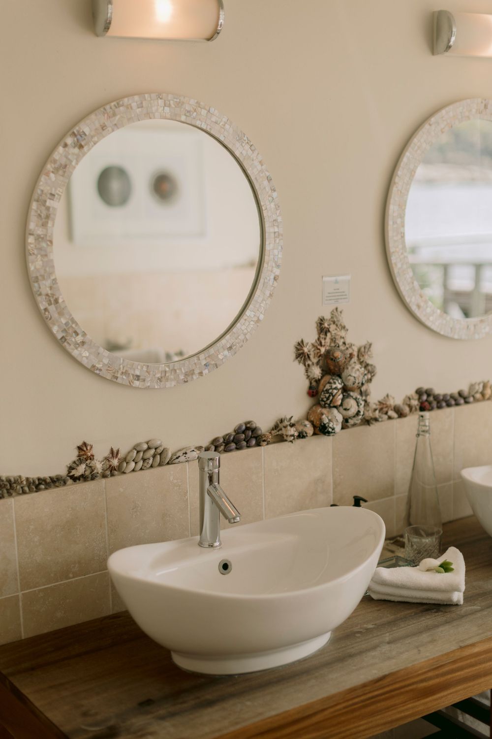 Elegant bathroom vanity with shell-framed round mirrors and white vessel sink on wood counter.