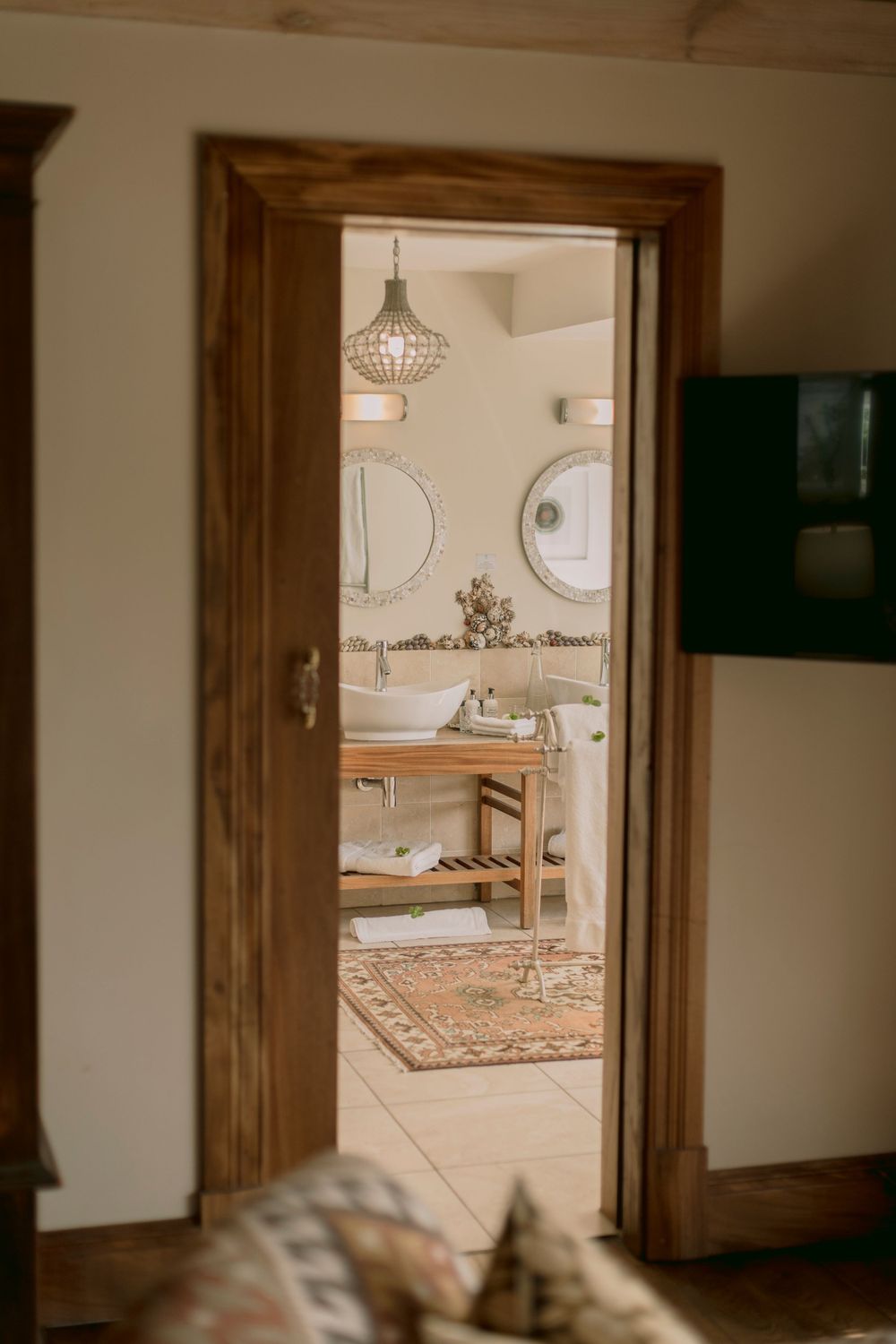 Elegant wooden doorway framing a stylish bathroom with round mirrors, vessel sinks, and decorative chandelier.
