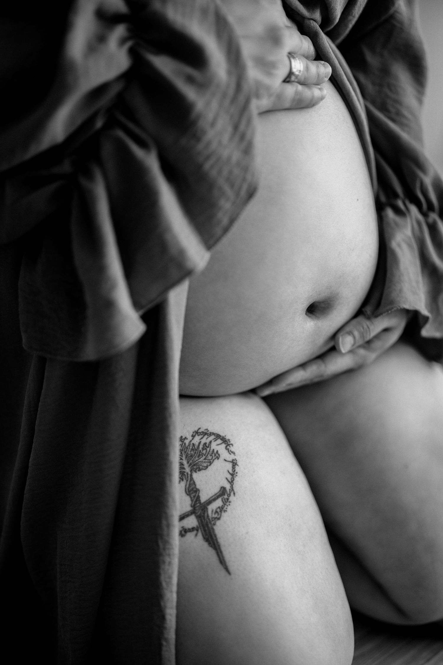 Black and white artistic maternity photo showing a bare pregnant belly and small tattoo design on the skin.