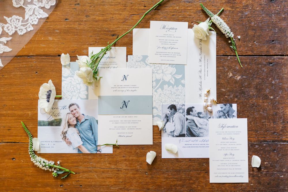 Wedding invitation suite with engagement photos and floral details laid out on rustic wooden table surface.