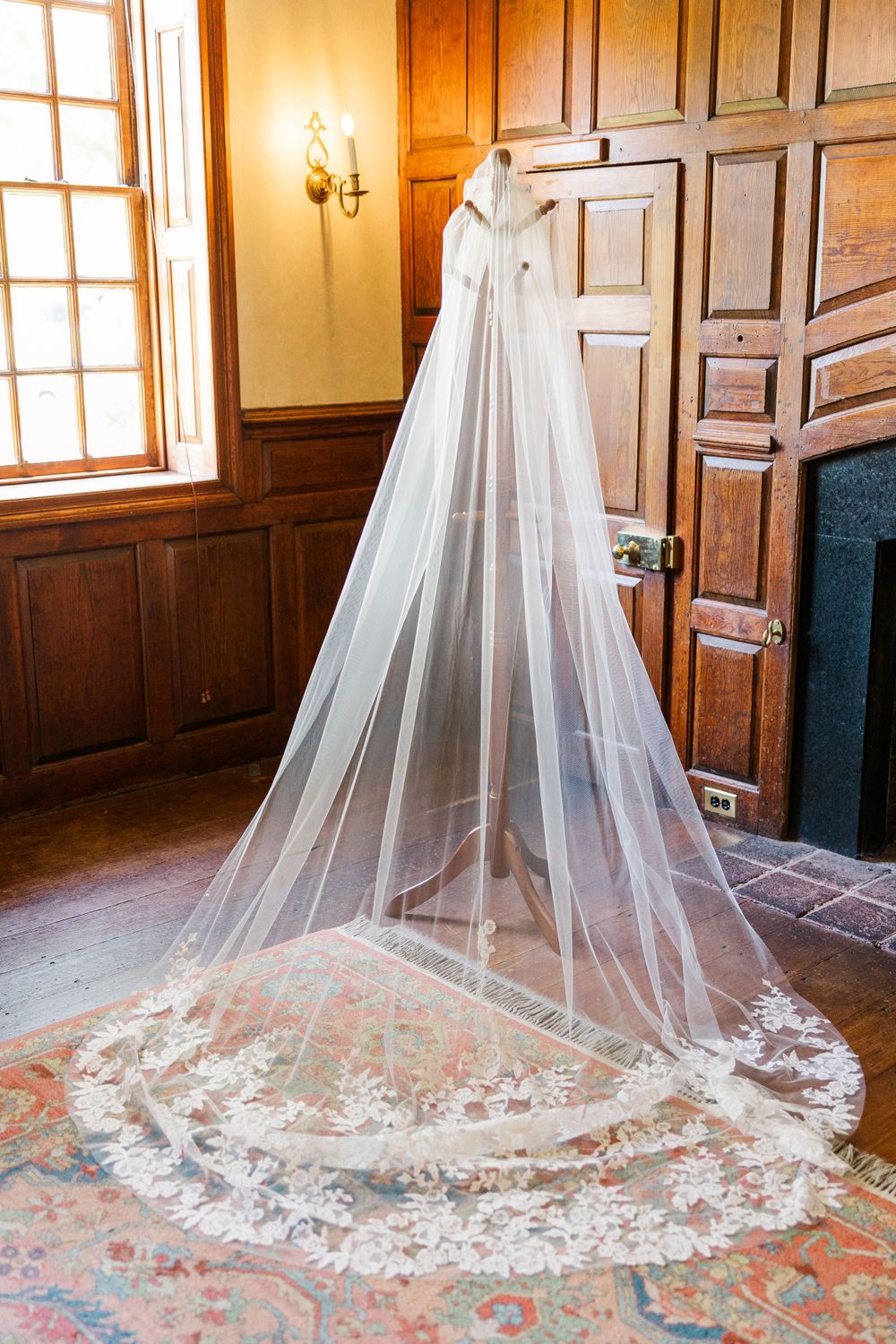 A flowing white wedding veil with delicate lace trim hangs on wooden paneled walls in warm lighting.