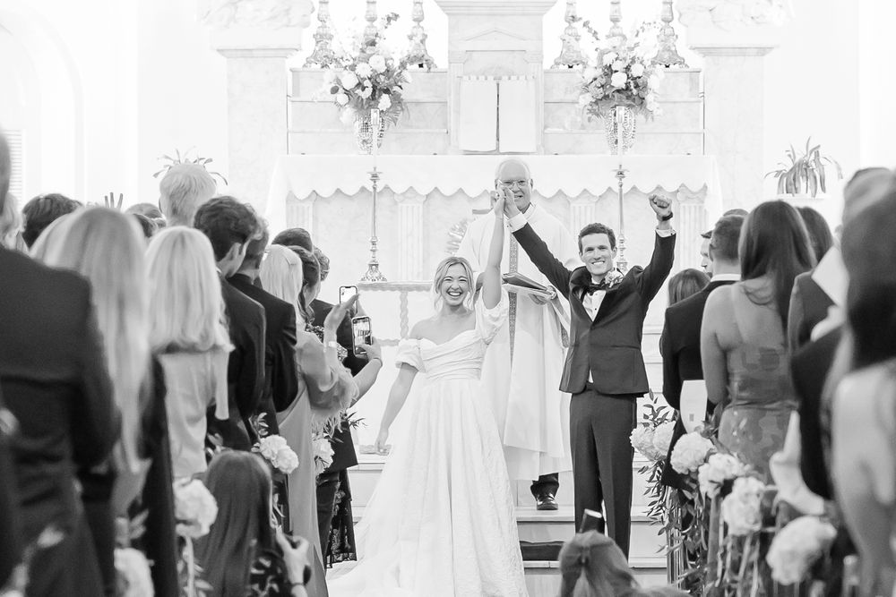 A joyful couple celebrate at the altar during their wedding ceremony as guests look on in black and white.
