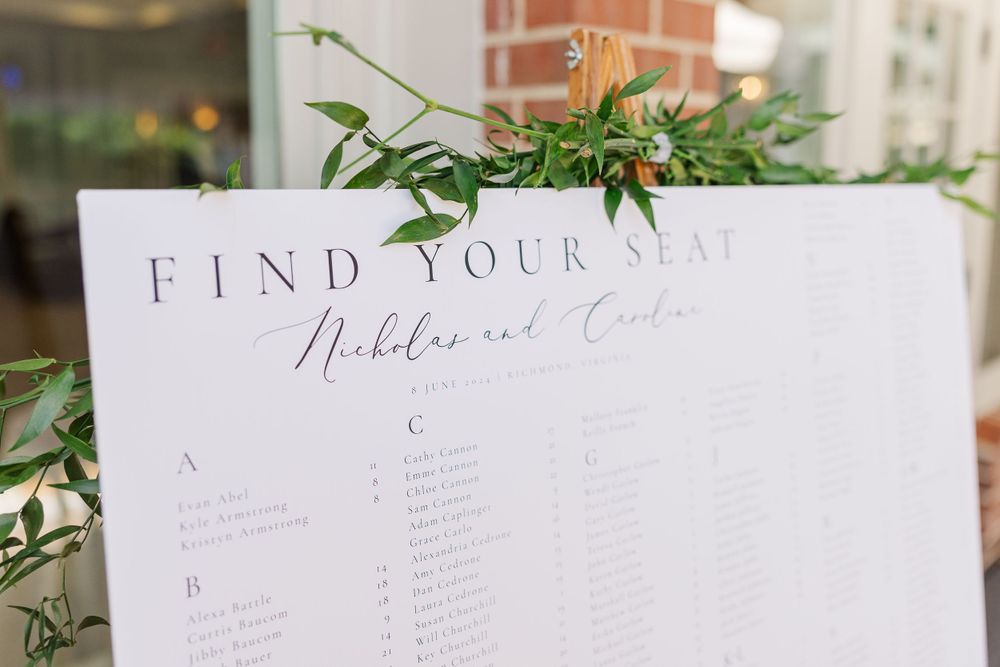 A wedding seating chart decorated with delicate greenery vines against a light pink wall.