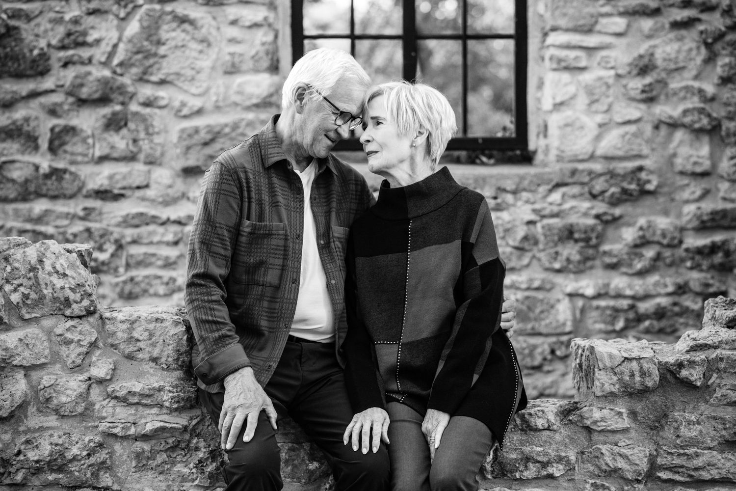 Black and white photo of a loving couple sharing an intimate moment together against a stone wall.