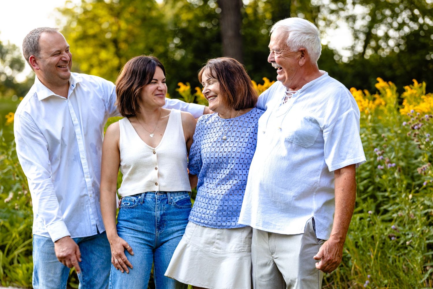 Happy family group smiling together outdoors in a field of yellow wildflowers on a sunny day.