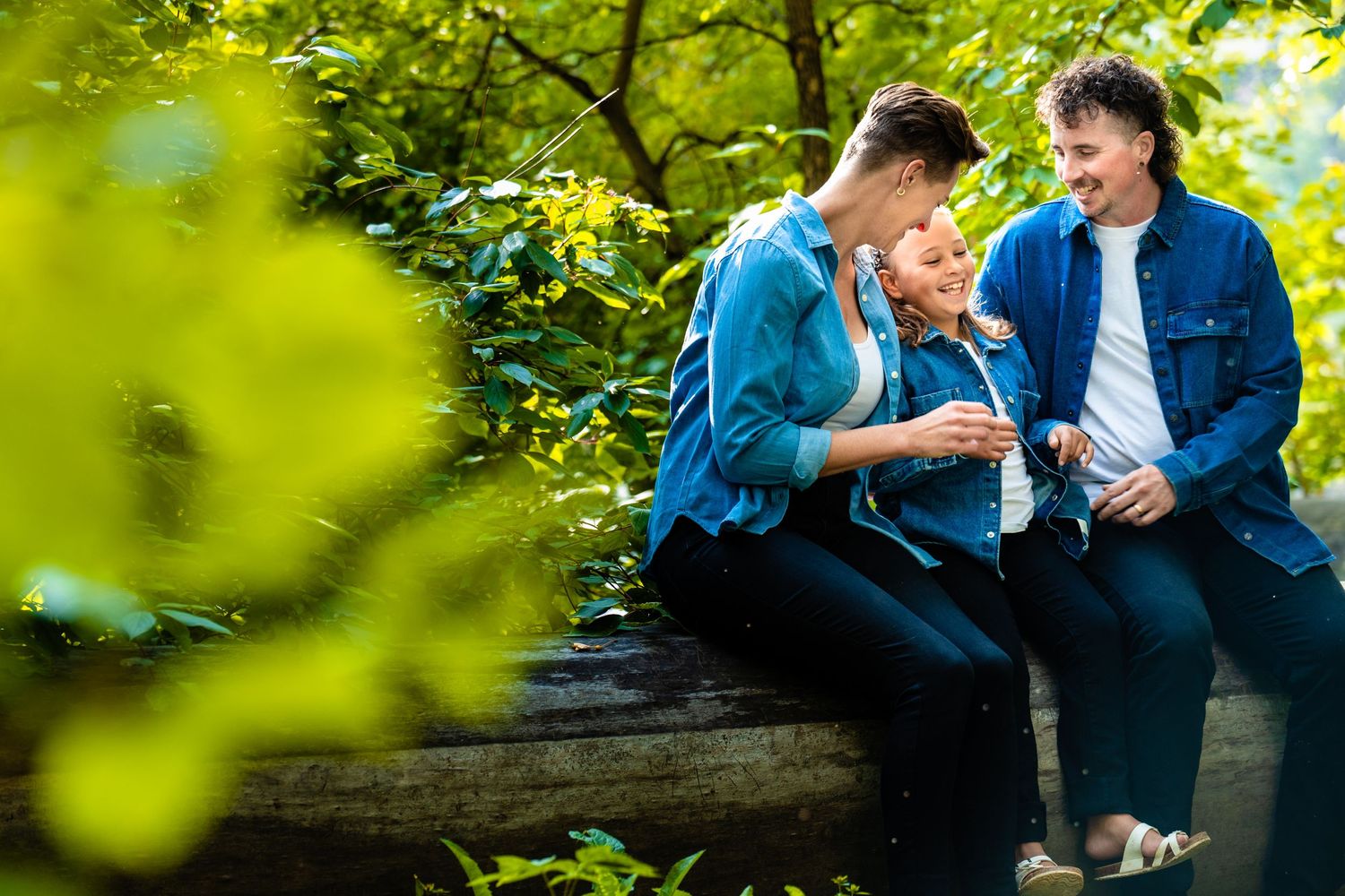 Three people sitting on a fallen log in a lush green forest setting sharing a happy moment together.