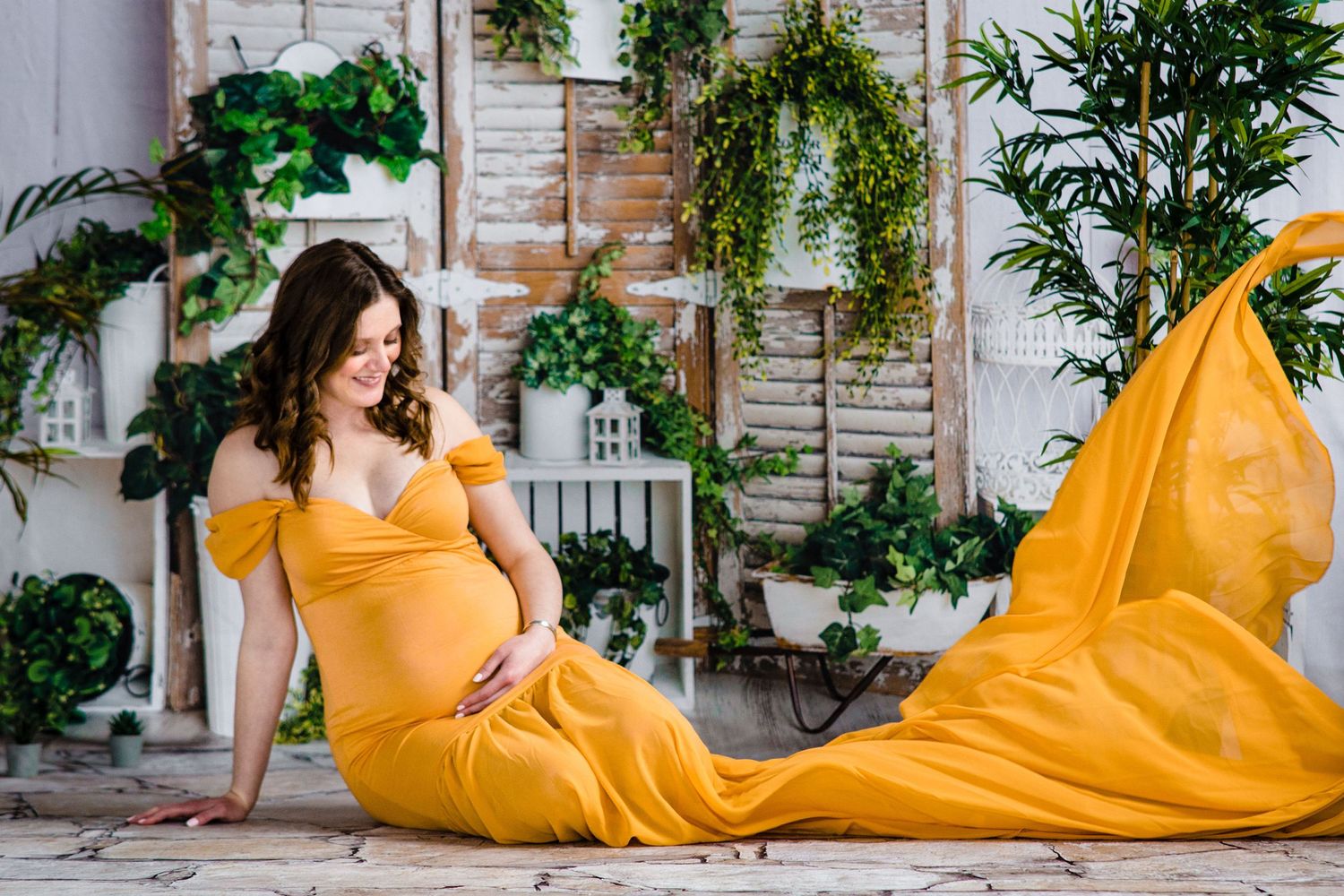 Flowing yellow dress contrasts beautifully against indoor botanical setting with white walls and cascading plants.