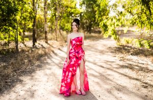 Full-length portrait of a person in a flowing red gown with thigh slit on a forest path.