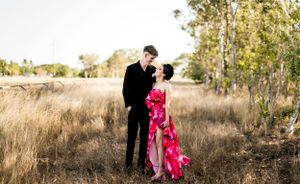 Romantic couple poses in formal attire against natural outdoor setting.