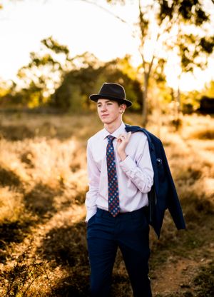 Relaxed formal wear featuring navy jacket, tie and fedora in warm evening light.