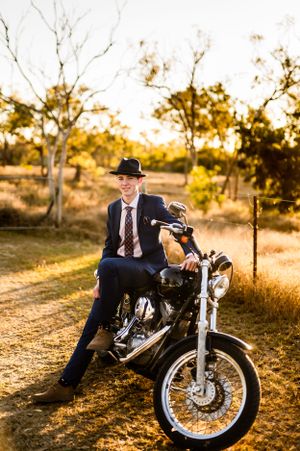 Vintage-inspired portrait of someone in a suit and fedora posing on a motorcycle at sunset.