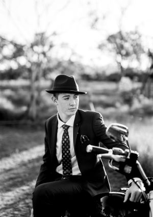 Classic black and white photo featuring a motorcycle rider in formal attire and fedora hat.
