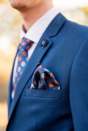 Close-up of a navy blue suit jacket with polka dot tie and matching pocket square showing fine tailoring details.