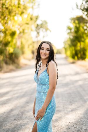 Woman in sequined blue dress poses on rural road during golden hour.