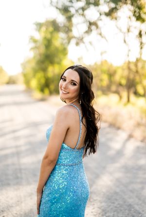 Woman in sparkly blue gown smiling over shoulder on country road.