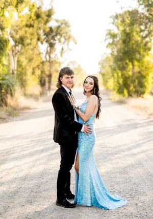 Couple in formal wear dancing together on a dirt road during golden hour.