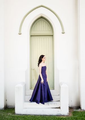 A structured navy blue evening gown photographed against white arched church architecture.
